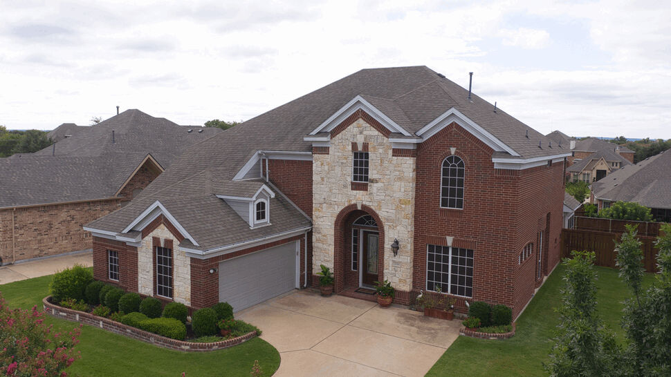 Front aerial roof inspection | US Metal Roofing Consortium Aerial front view of a two-story brick home with pitched roof and driveway.