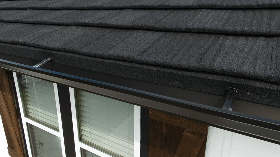 Close-up of textured black metal roof tiles and a gutter above a window.
