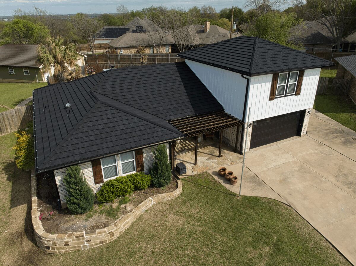 Aerial view of a house with a black metal tile-style roof and landscaped yard.