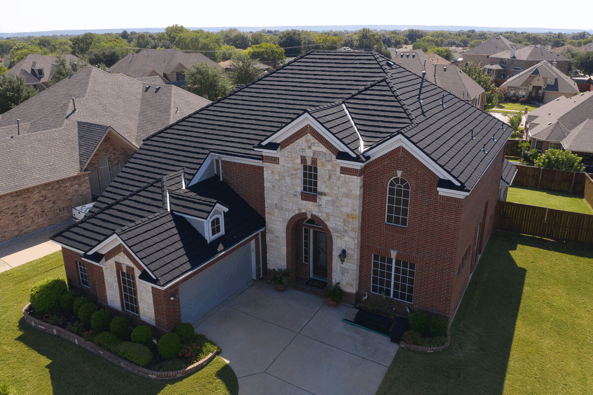 Aerial view of two-story brick house with black Hurricane Shake Pro metal roof.