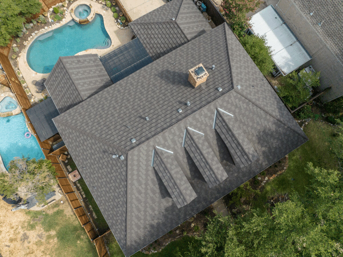 Drone view of a large home's dark metal roof and backyard pools