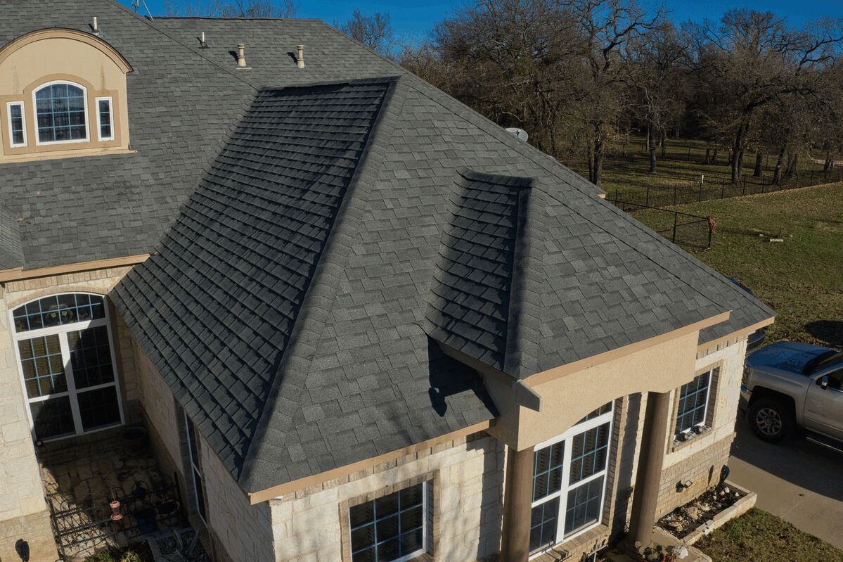 Aerial view of a residential shingled roof and front windows with surrounding yard