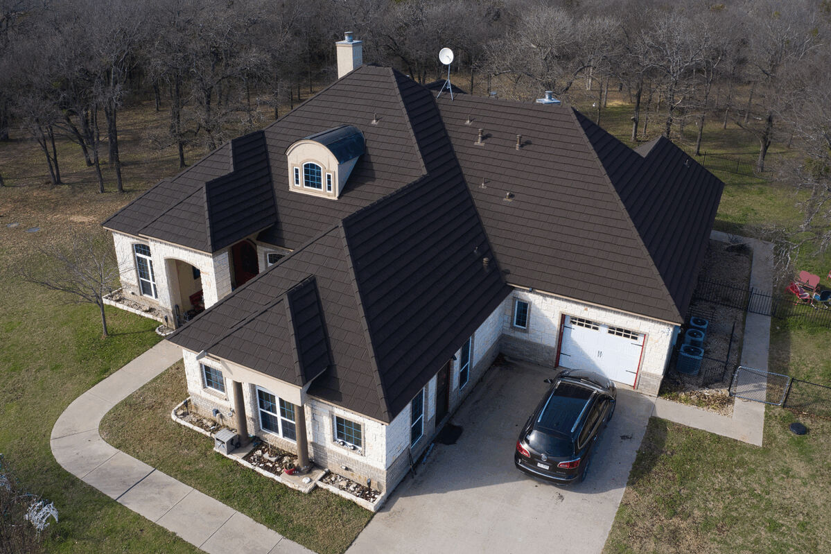 Aerial view of a large house with dark brown metal roof and driveway.