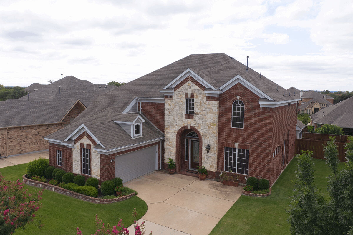 Aerial front view of a two-story brick home with pitched roof and driveway.