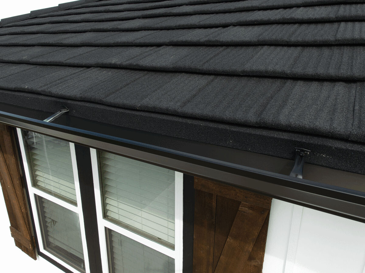 Close-up of textured black metal roof tiles and a gutter above a window.