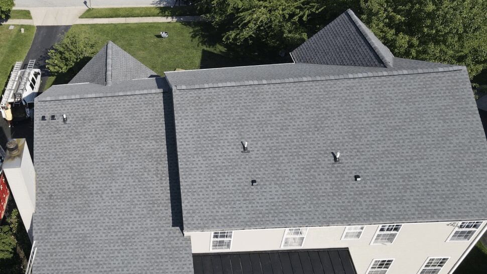Aerial close-up of a gray asphalt shingle roof with vents and multiple ridgelines.