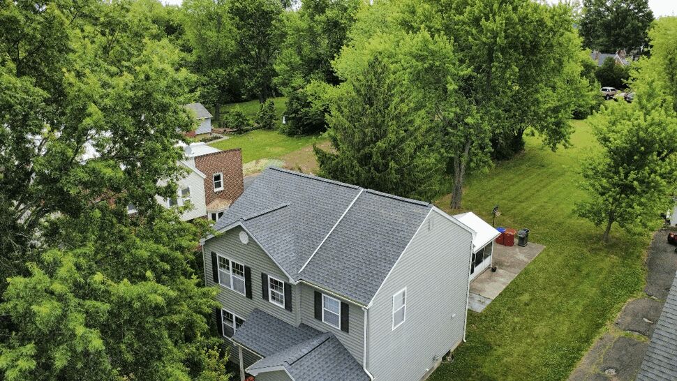 Aerial view of a gray shingle roof on a two-story house surrounded by trees.