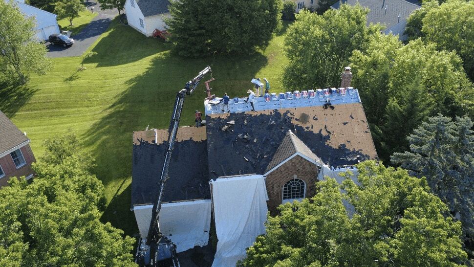 Aerial view of crew removing old shingles with a crane on a residential roof.