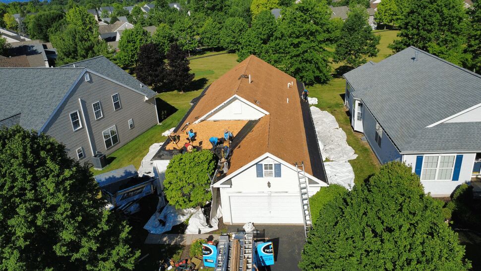 Aerial view of crew removing shingles from a house roof.