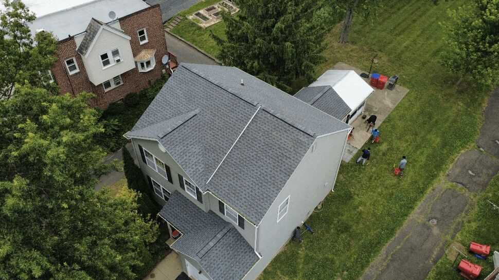 High-angle view of house siding and roof with yard and crew visible below.