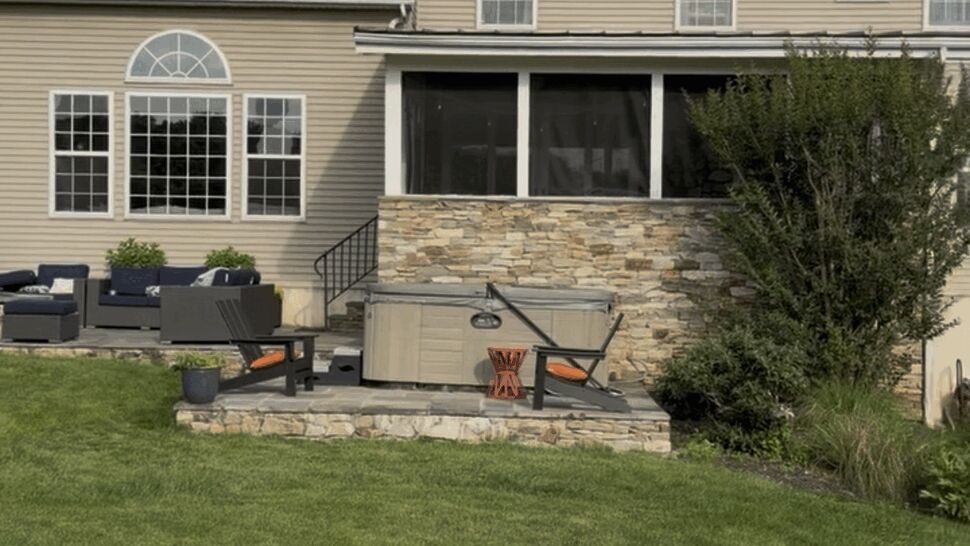 Backyard patio area with hot tub, stone retaining wall, and screened porch on beige siding.