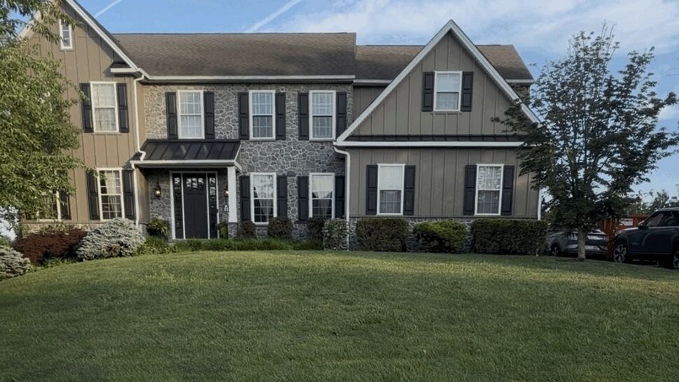 Two-story colonial home with stone and vertical siding and a Paramount sign on the lawn.