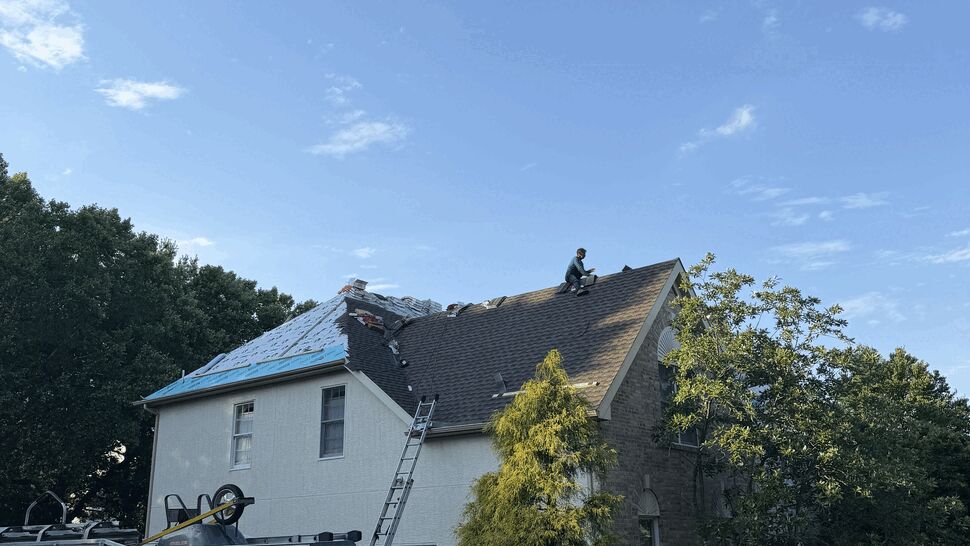 Service van and ladder beside home while a worker installs roofing