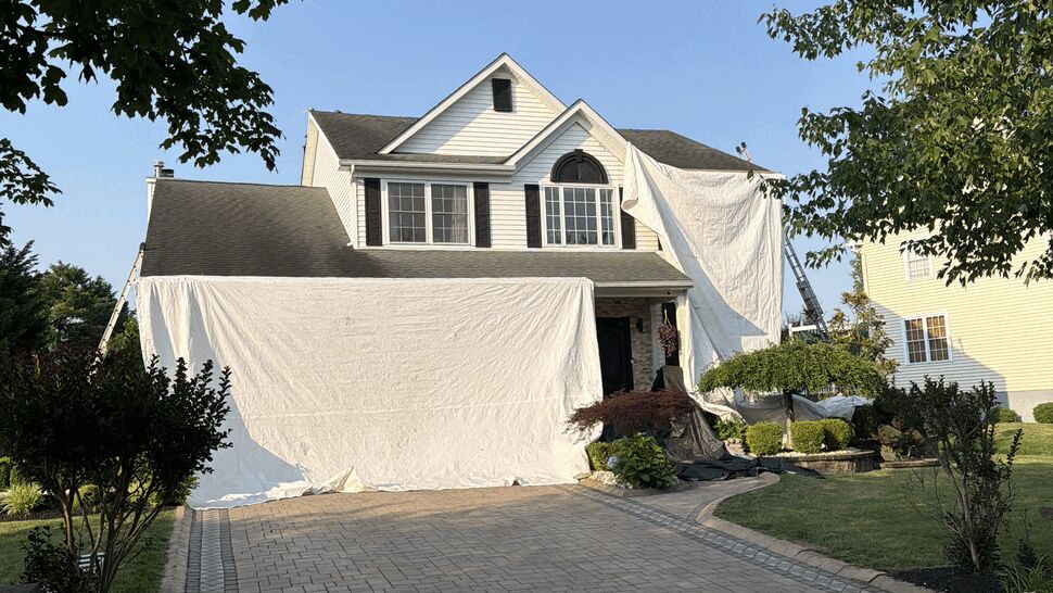 Two-story house with large white tarps covering front and driveway during roof work.