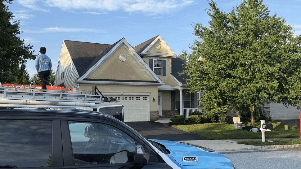 Paramount Home Solutions truck parked in front of house while a worker stands on the roof.