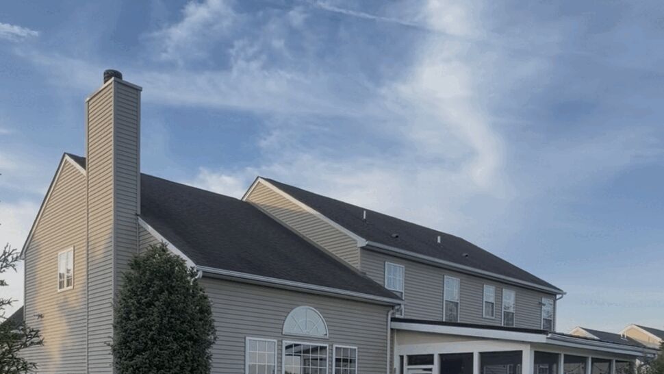 Rear view of home with large arched window, screened porch, and asphalt shingle roof.