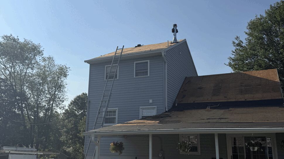 Two-story house with roof tear-off, ladders and roofing debris in the yard.