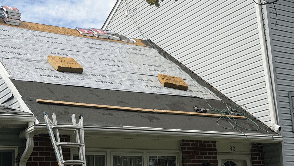 Close view of roof underlayment with bundles of shingles and a ladder to the porch roof.