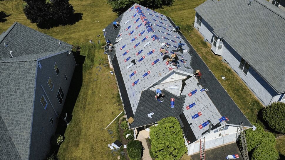 Workers installing roof underlayment on a home roof.