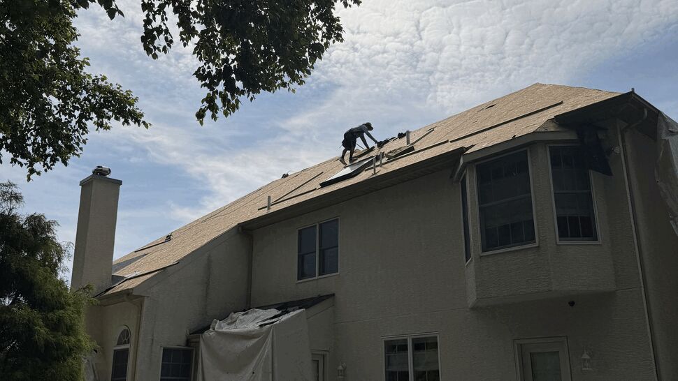 Roofer working on steep roof slope above a tarp-covered deck