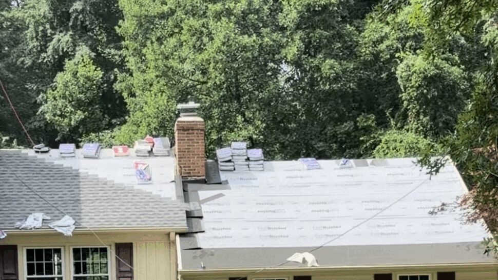 Roof underlayment with stacked shingle packs near the chimney ready for installation.