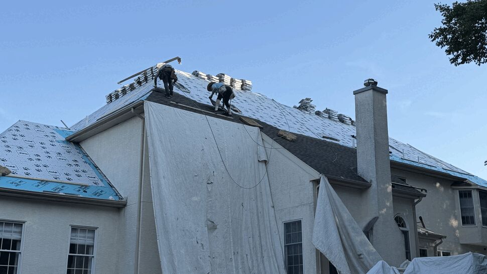 Two roofers installing underlayment and stacking shingles on the ridge