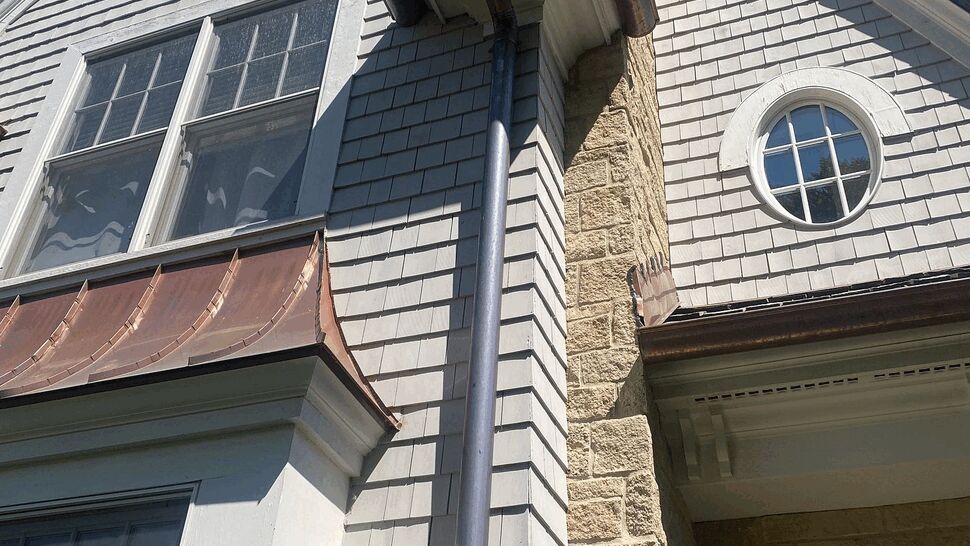 Bay window with a curved copper awning and adjacent downspout