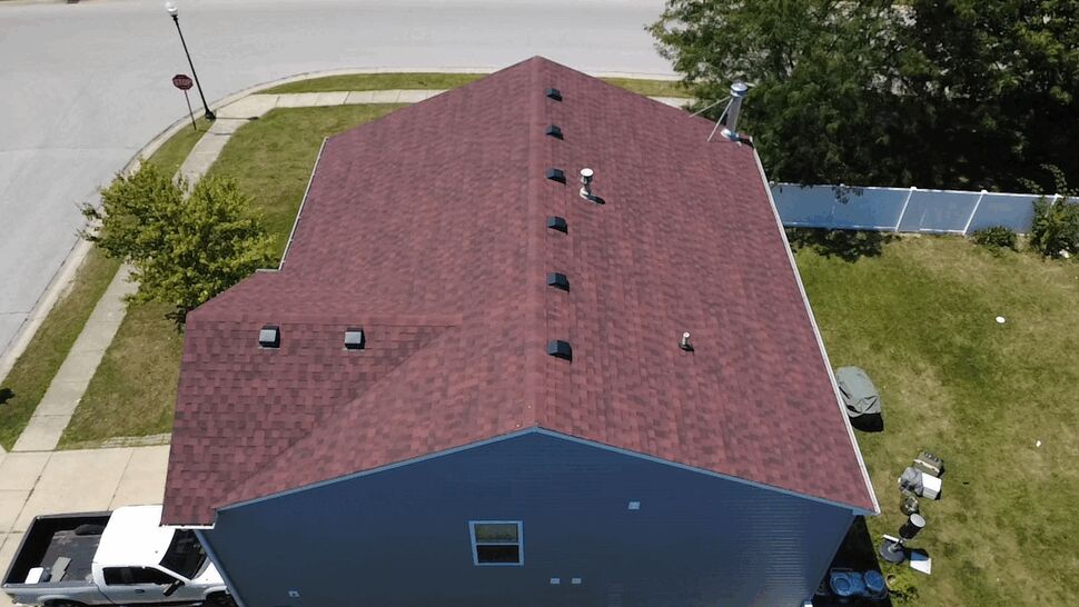 Aerial view of a red shingle roof ridge with vents and driveway below