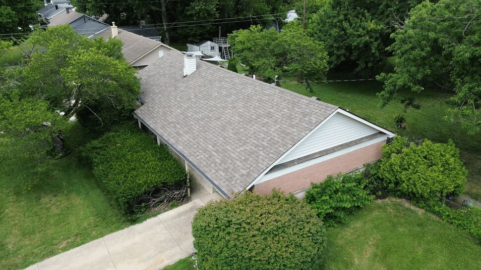 Angled drone view of a light-gray shingle roof and surrounding yard.