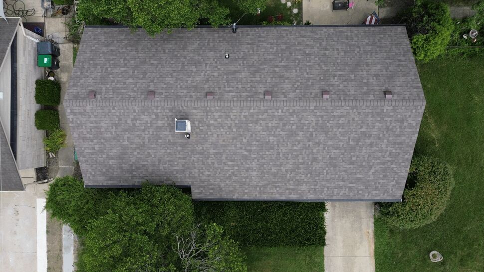 Top-down aerial of a uniform gray shingle roof with vents and driveway visible.