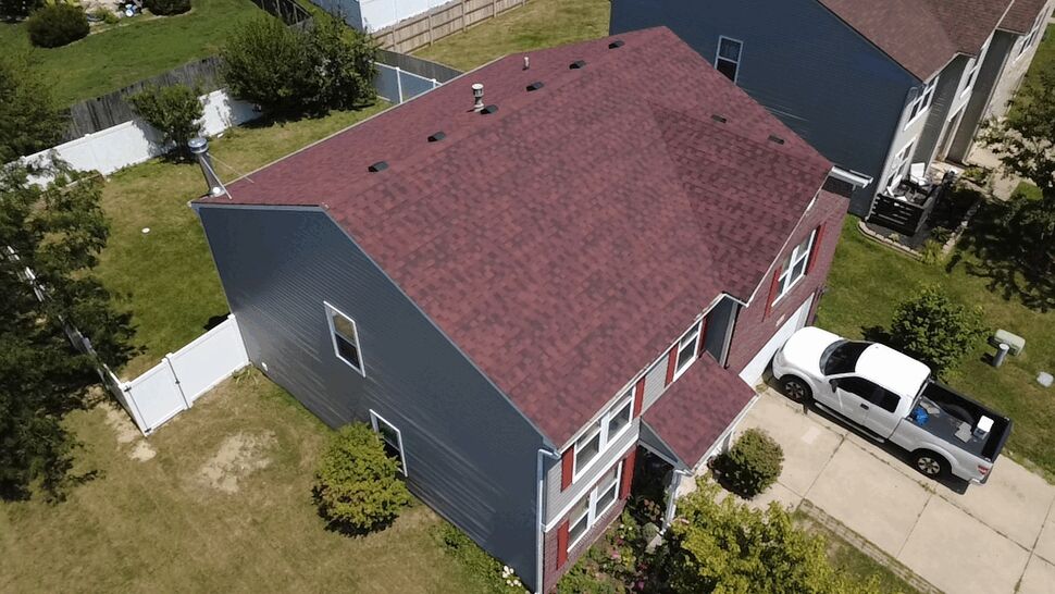 Angled aerial of two-story home with grey siding and red shingle roof