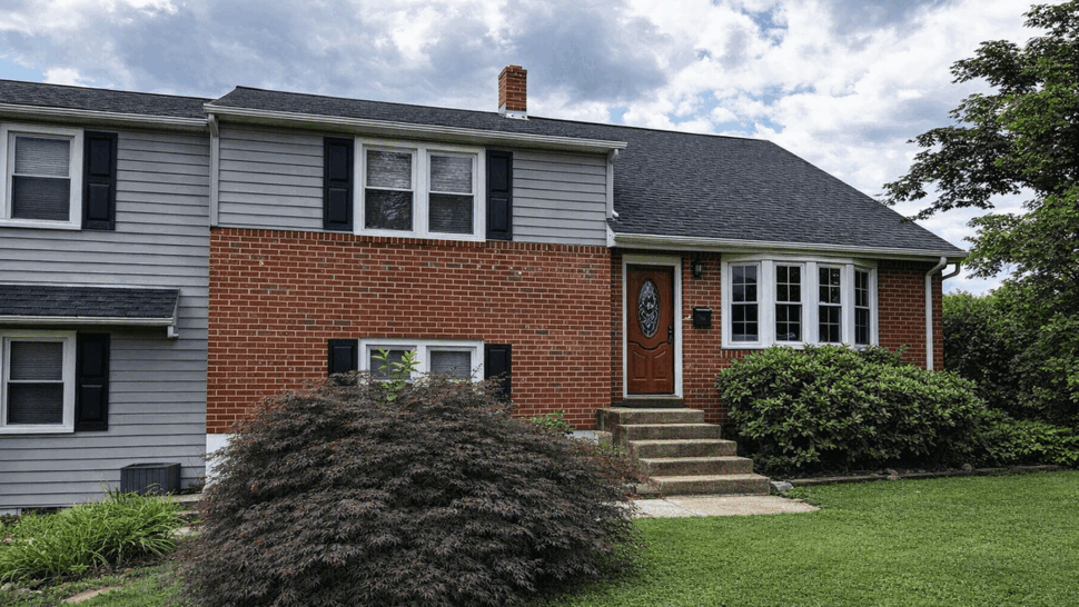 Front of brick and gray sided house with dark shingle roof and wooden entry door