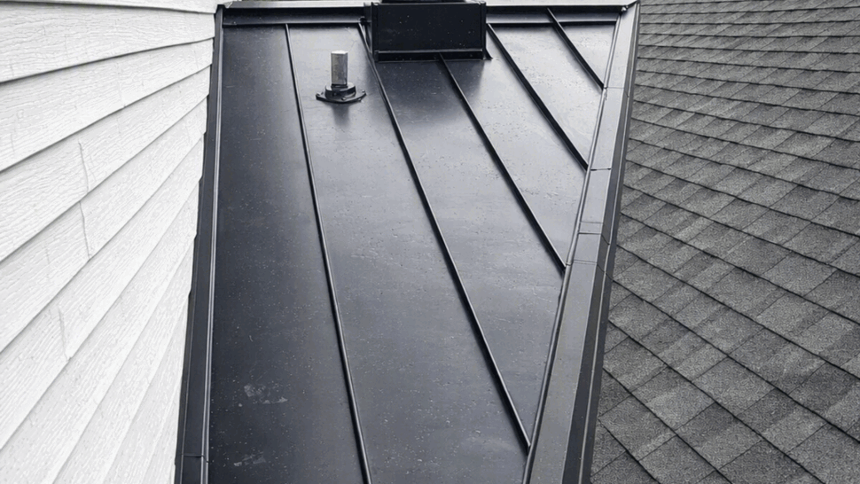 Triangular metal roof valley between house walls with roof vent pipe