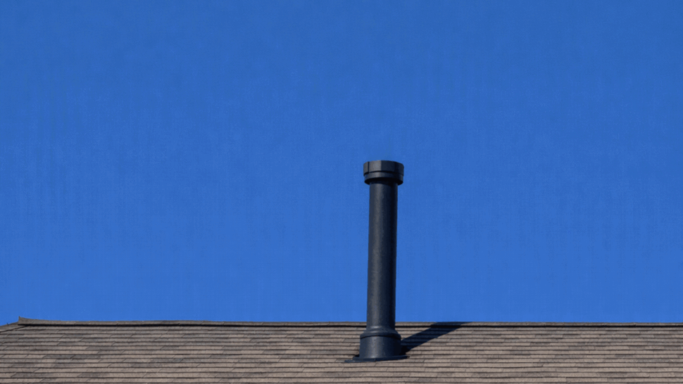 Shingled roof with black vent pipe and gutter along eave under blue sky