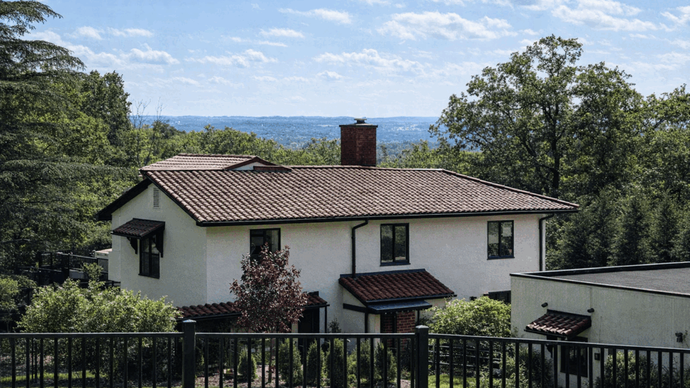 Two-story stucco home with red Spanish tile roof and surrounding trees