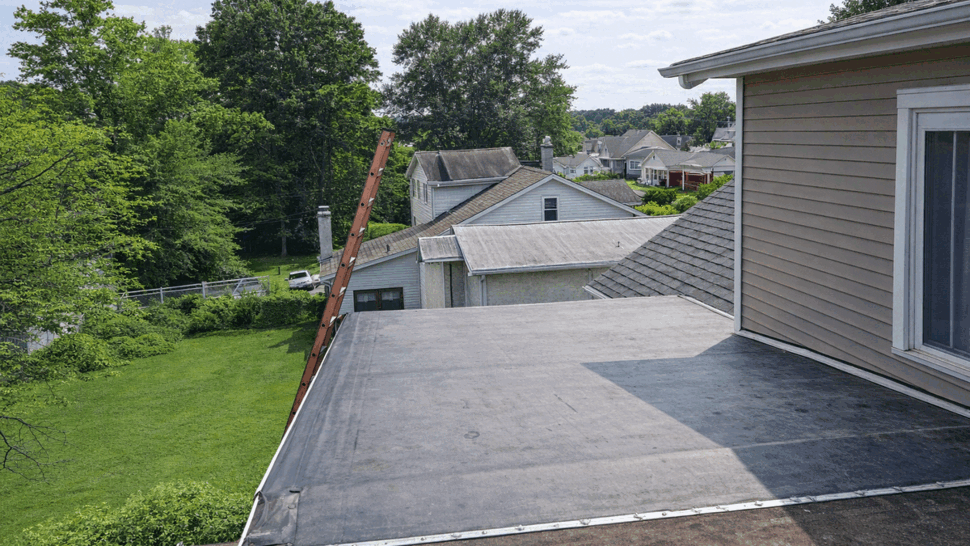 Aerial view of a low-slope flat roof and ladder overlooking a neighborhood