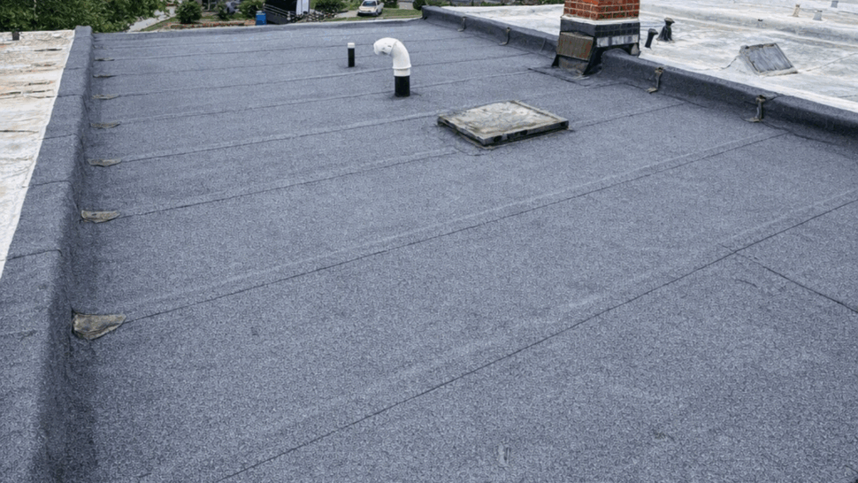 Flat commercial roof with mineral-surfaced membrane, vents, and surrounding rowhouses.