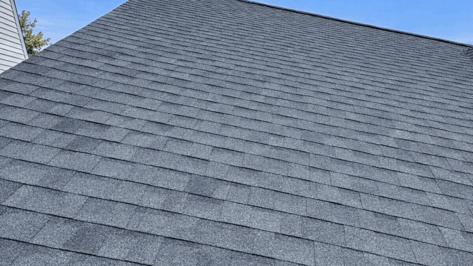 Close-up view of dark gray asphalt roof shingles under a blue sky.