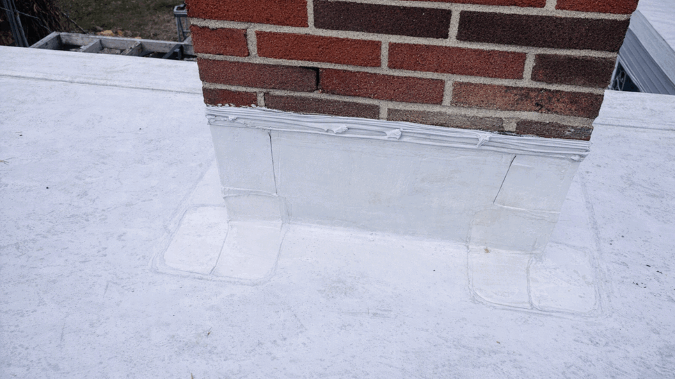 Chimney Base Flashing Repair | Tycos Roofing And Siding Inc Close-up of patched chimney base flashing on white roof membrane
