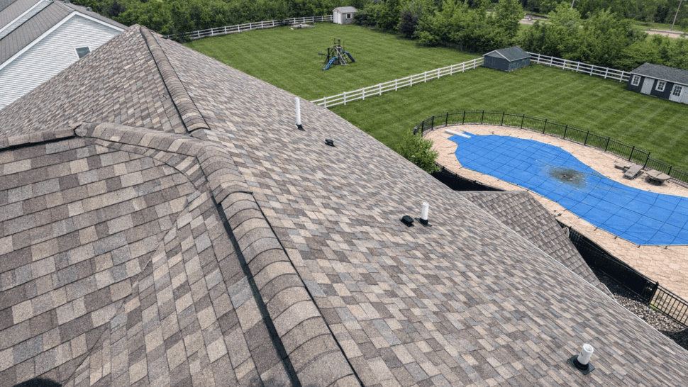 Shingled roof ridge and vents above a backyard pool and fenced yard.