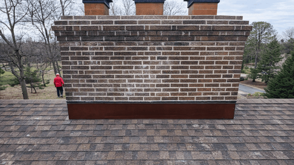 Brick chimney with new metal flashing at its base on shingled roof