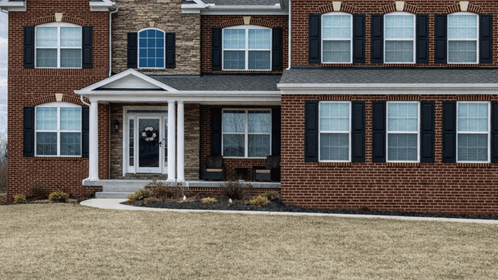 Large two-story brick colonial home with front porch and lawn
