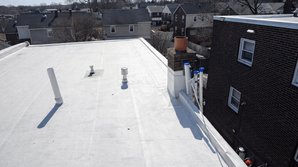 White flat roof with chimney, vents and neighboring houses in background.