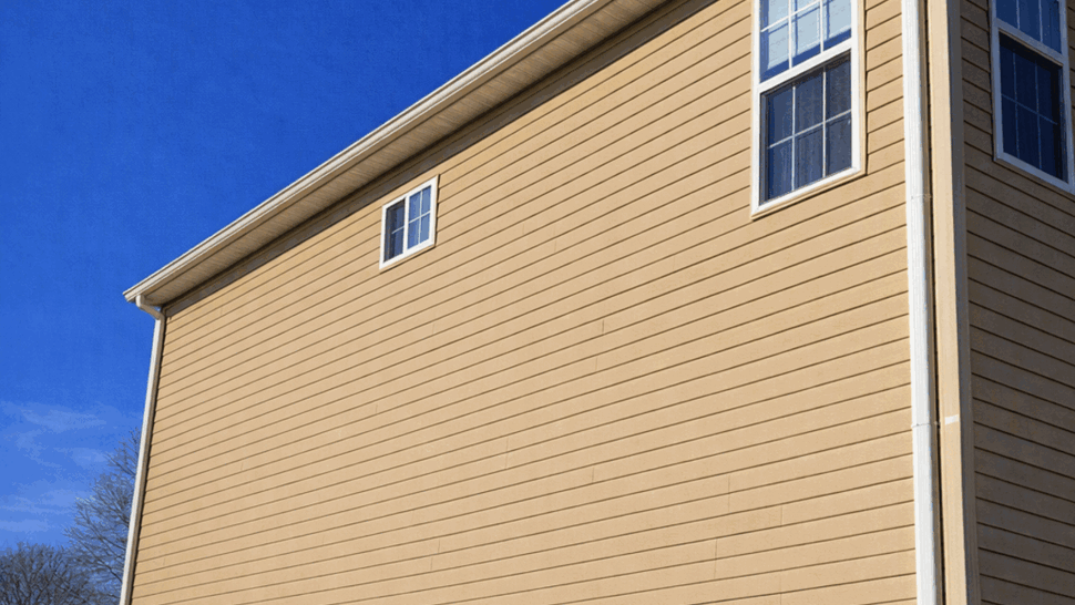Beige vinyl siding with white downspout under blue sky