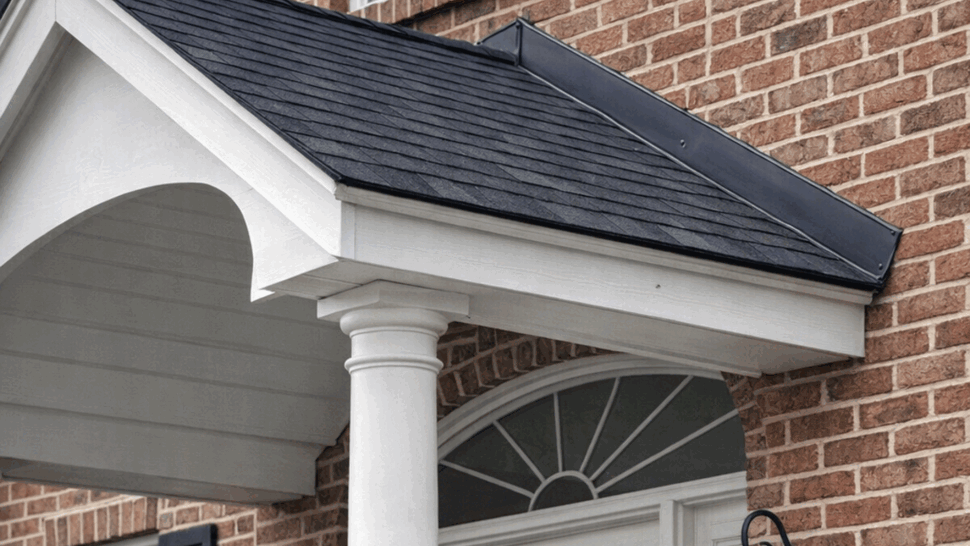 Close-up of brick entry with small shingled porch roof, white column, and lanterns