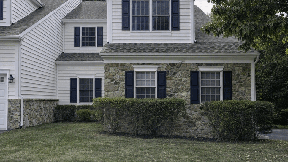 Two-story home with white siding, stone facade, black shutters and a shingled roof.