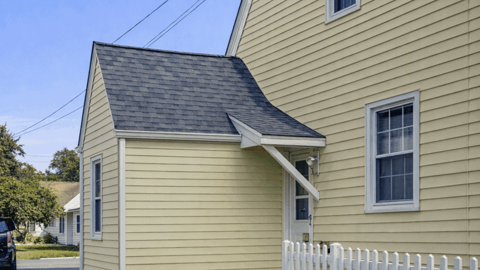 Side view of a pale green home with gray roof shingles and siding