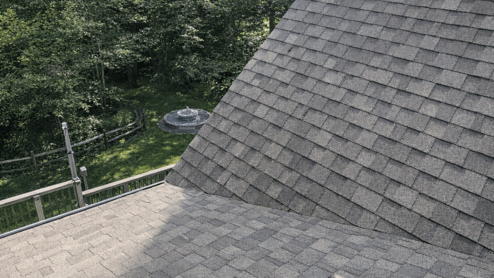 Close-up of asphalt shingle roof slope near a chimney looking toward trees.