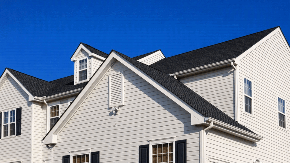 Close-up of gable roofline, gutters and white vinyl siding under blue sky