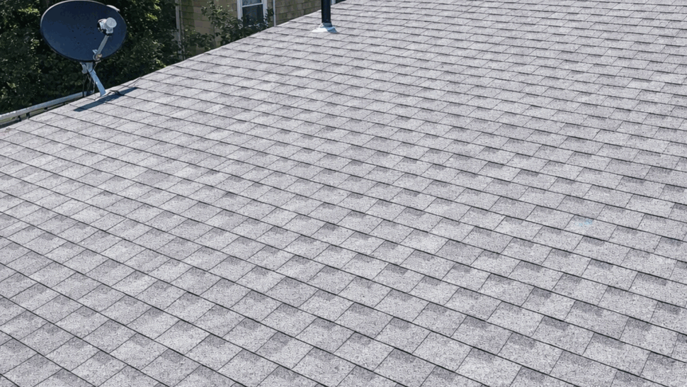 Close view of gray asphalt roof shingles surrounding a dormer and vent